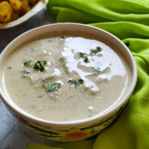 cucumber raita served in a white bowl kept on a green cloth