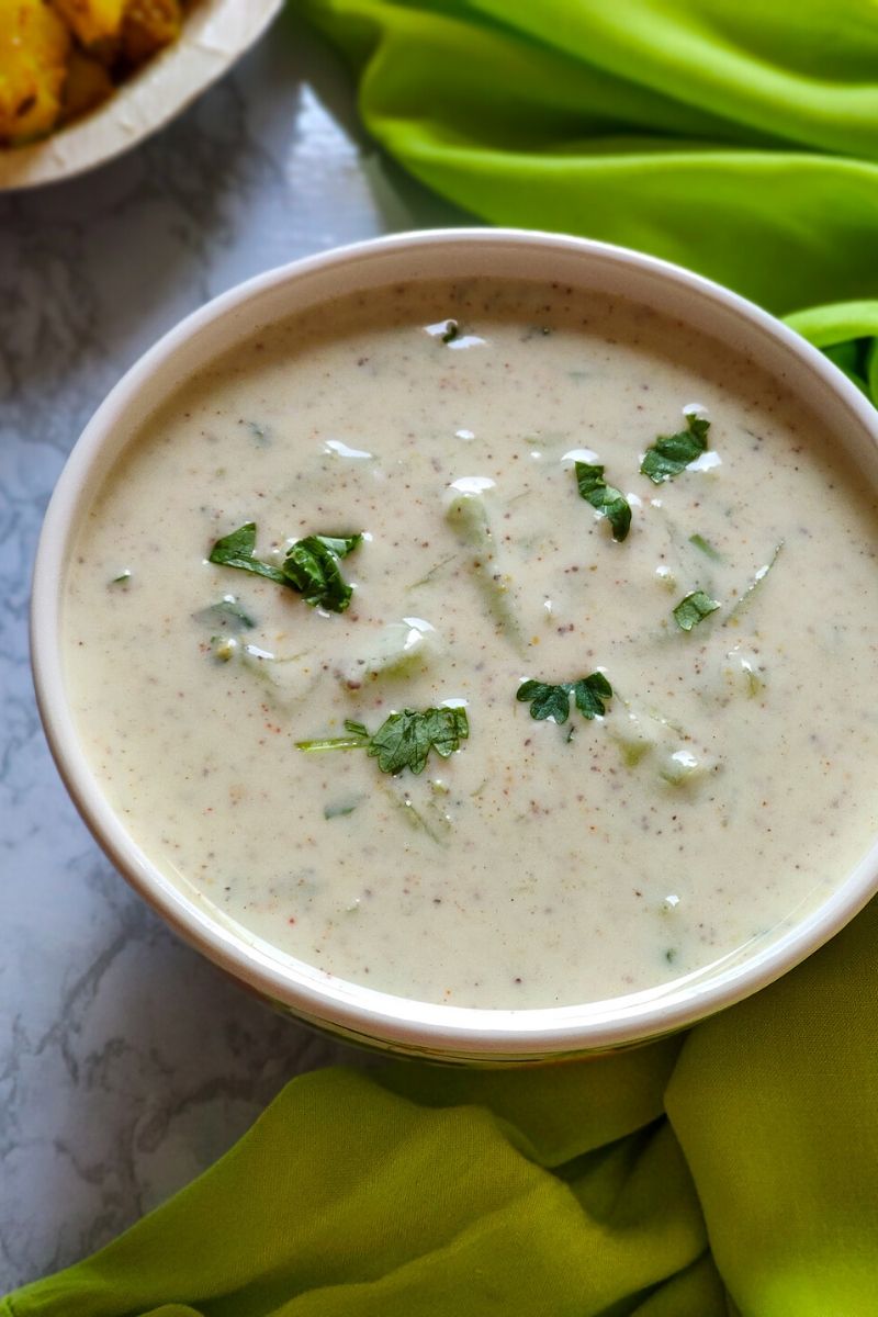 cucumber raita served in a white bowl kept on a green cloth