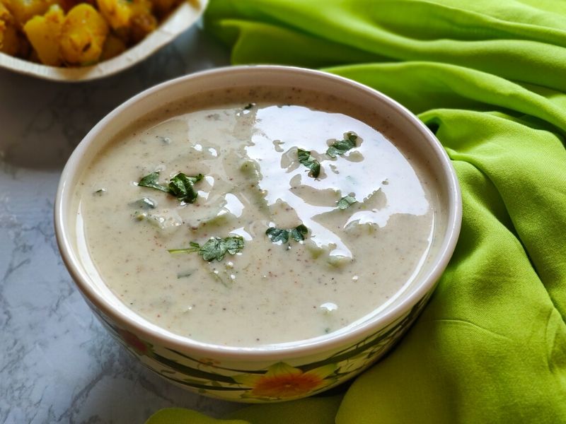 cucumber raita served in a white bowl kept on a green cloth