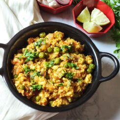 Paneer bhurji served in a black wok with lime wedges and onion slices