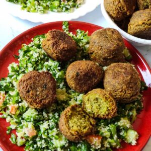Vegan snack falafel served over Tabbouleh on a red plate with more salad and falafel in the background