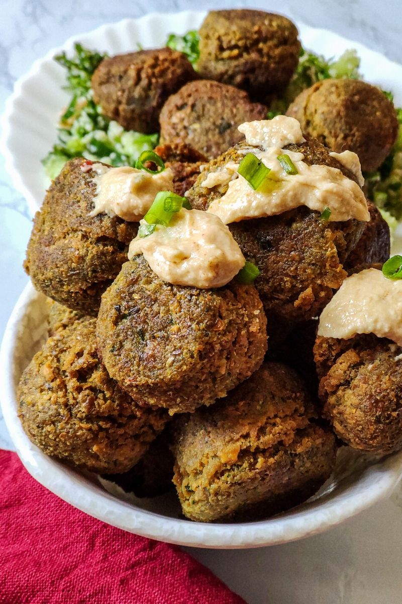Falafel drizzled with hummus and garnished with chopped parsley served in a white bowl