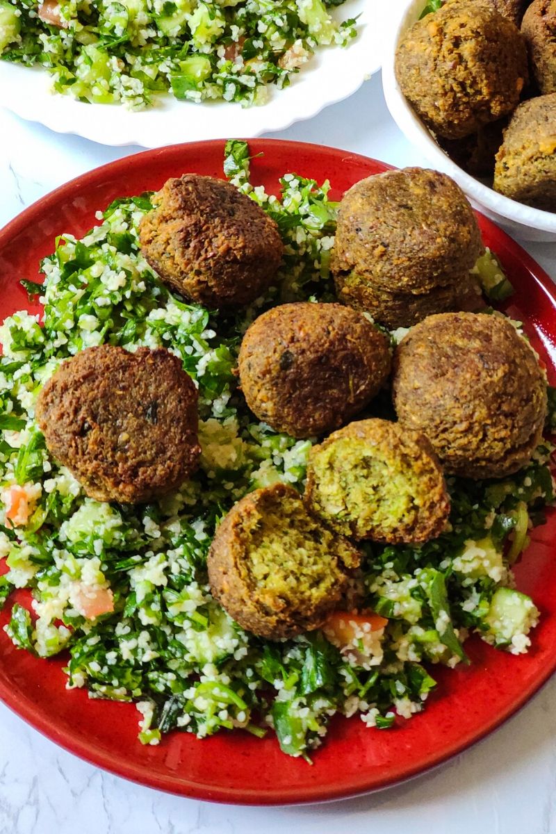 Vegan snack falafel served over Tabbouleh on a red plate with more salad and falafel in the background