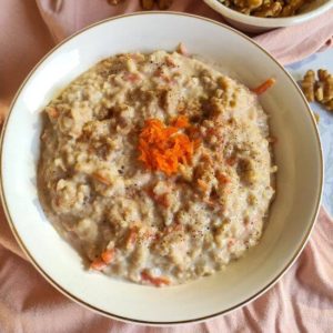 Carrot cake oats garnished with grated carrot served in a white bowl with walnut kernels in the background