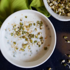 A bowl of sprouts raita with a bowl of mung bean sprouts in the background