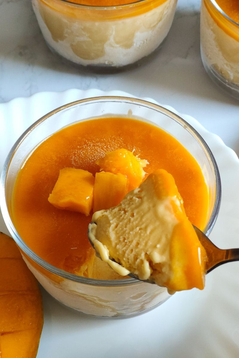 A spoon full of mango cheesecake ice cream scooped out from a glass bowl of ice cream