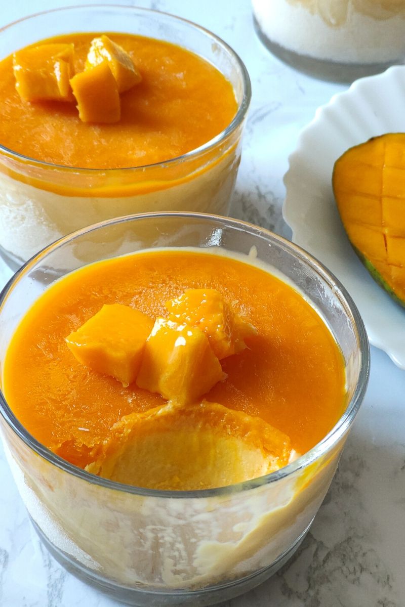 A spoon full of mango cheesecake ice cream scooped out from a glass bowl of ice cream