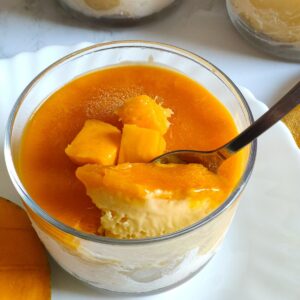 A spoon full of mango cheesecake ice cream getting scooped out from a glass bowl of ice cream,