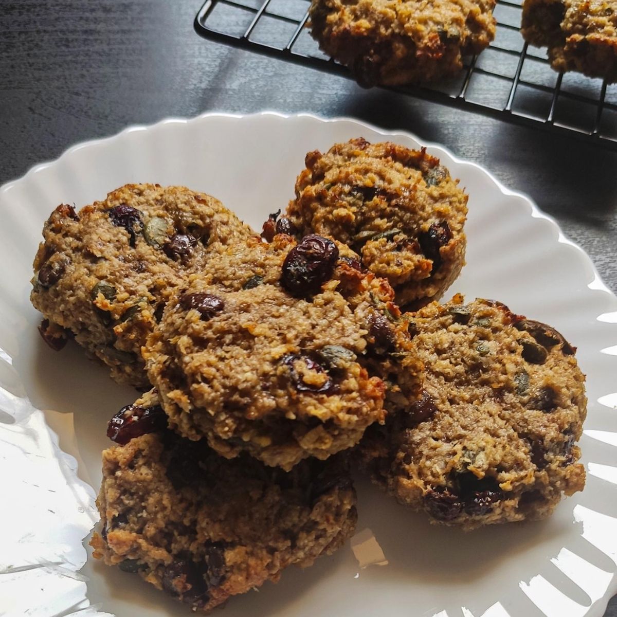 Four vegan oatmeal cookies on a white plate more cookies in the background