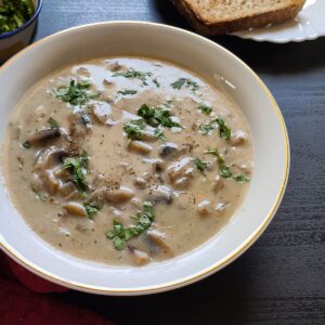 Vegan mushroom soup served in a white bowl with bread in the background
