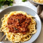 vegan bolognese sauce served on top of cooked pasta kept on a grey bowl