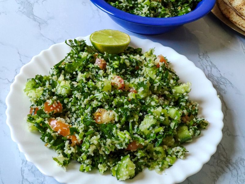 Middle Eastern Salad Tabbouleh serve on a white plate with a lime wedge on top another blue bowl of salad in the background