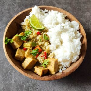 Tofu Thai green curry served in a wooden bowl with rice and garnished with a lime wedge