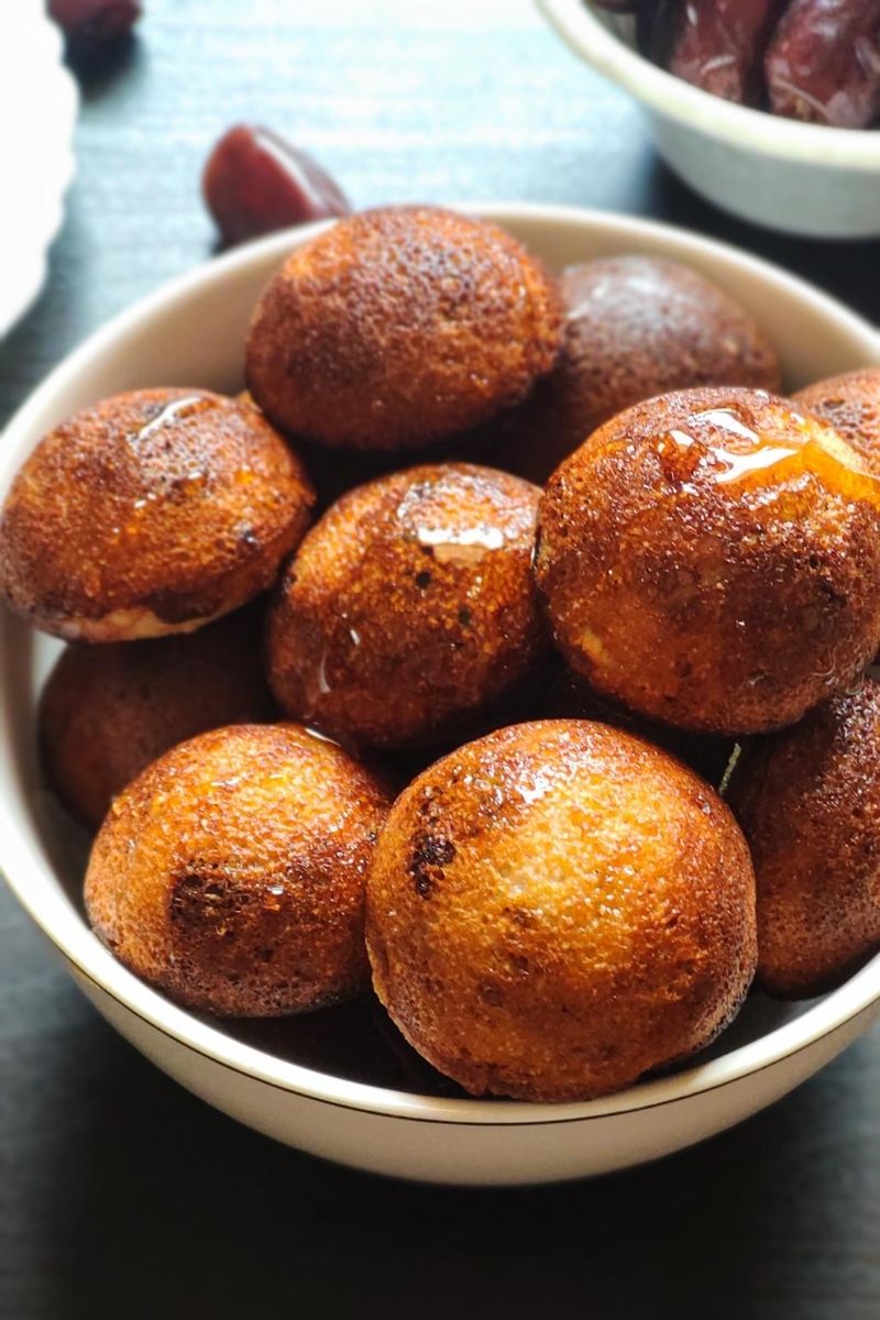 Sweet paniyaram served in a white bowl with some dates in the background