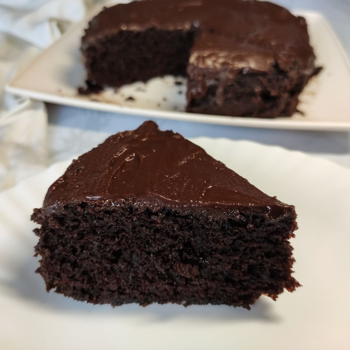 a slice of vegan chocolate cake served on a white plate more cake in the background