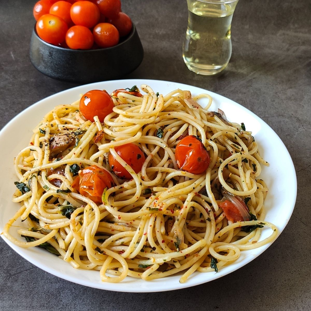 Cherry tomato pasta served in a white plate with a bowl of tomatoes and olive oil in the background