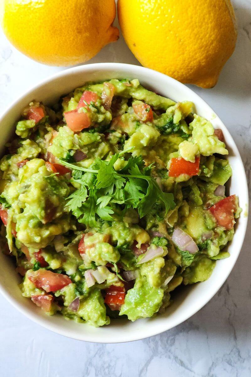 Guacamole in a white bowl with two lemons in the backgrouns