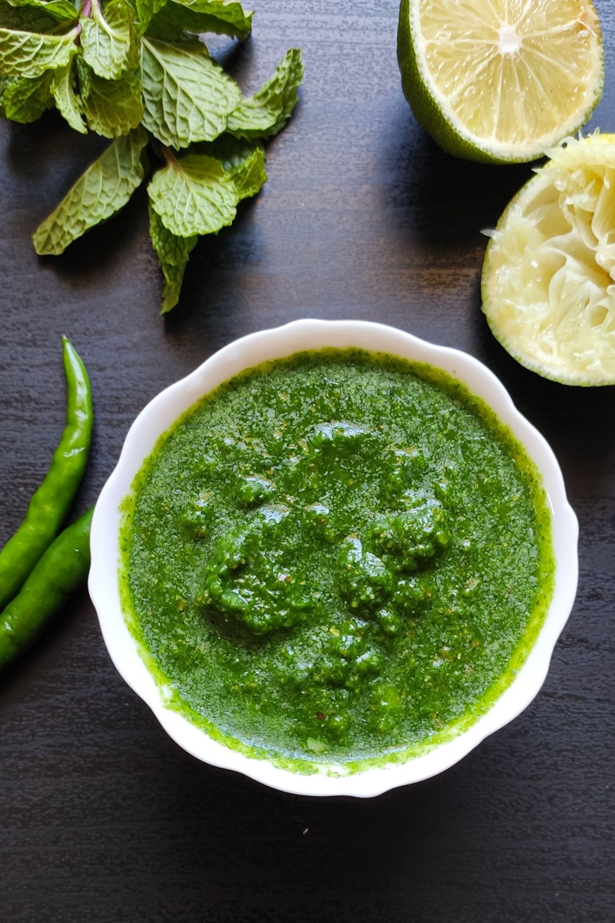 Mint chutney in a small bowl with mint leaves, lime and green chilies in the background