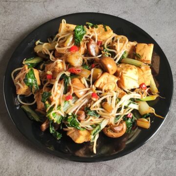 Chinese stir fried tofu with bean sprouts and mushrooms on a black plate