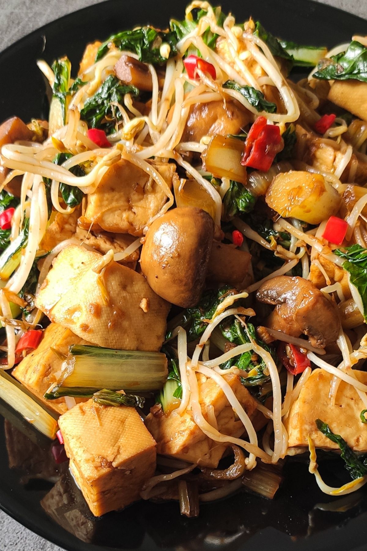 Tofu stir fry with mushrooms and bean sprouts on a black plate