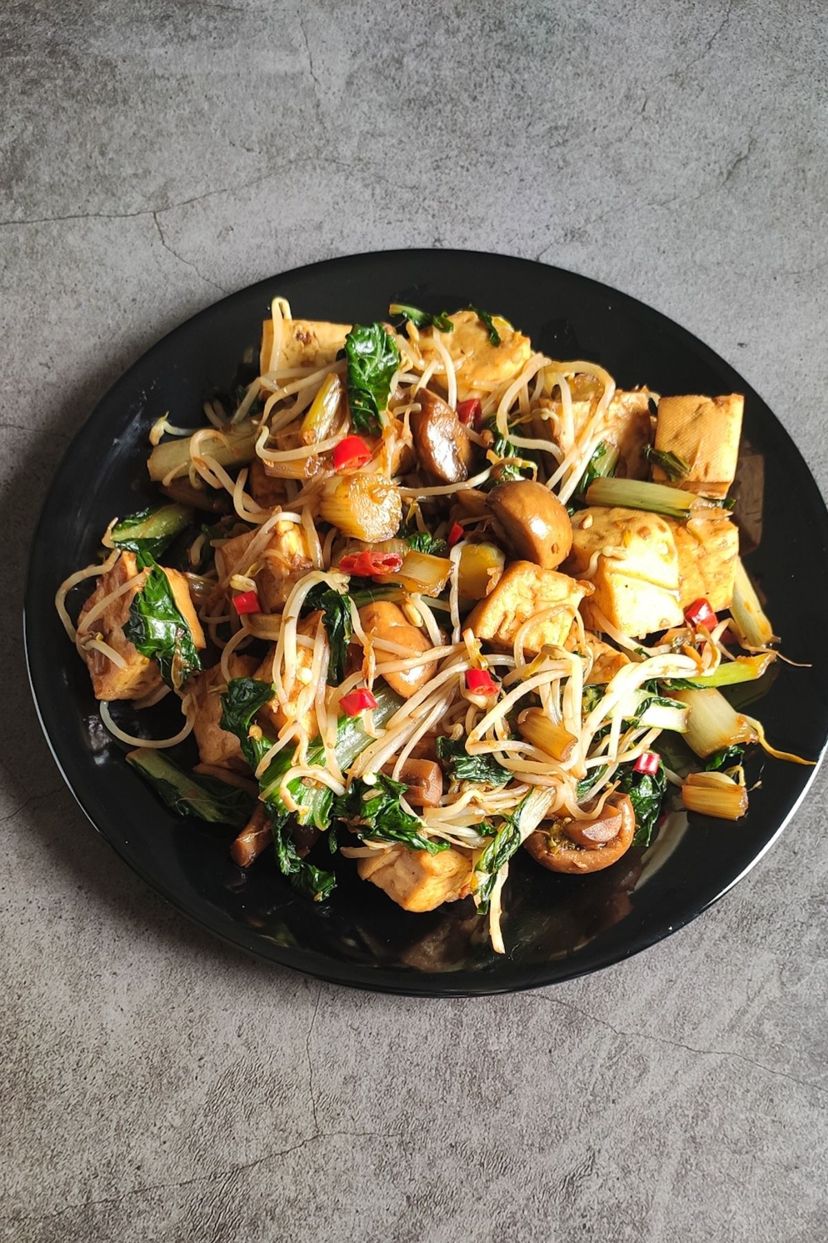 Stir fried tofu with mushrooms and bean sprouts on a black plate