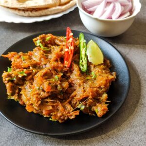 baingan bharta served on a black plate with roti and salad in the background