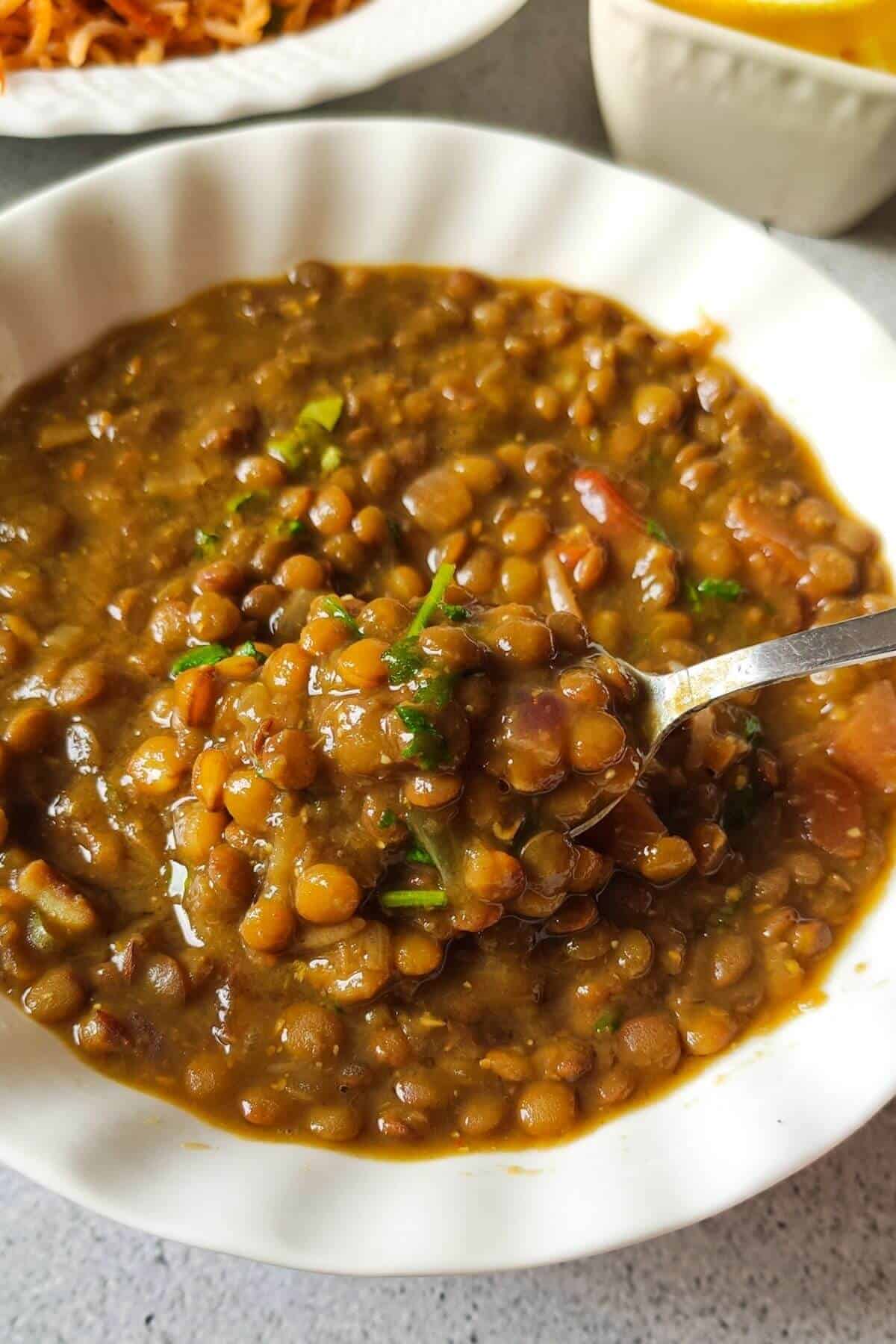 brown lentil curry getting scooped out of a bowl with spoon