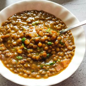 Brown lentil curry served in a white bowl and a spoon