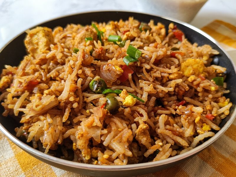 tofu fried rice served in a black pan kept on a table napkin with yellow and white checks