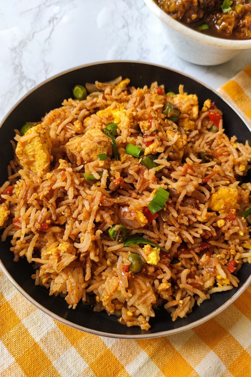 tofu fried rice served in a black pan kept on a table napkin with yellow and white checks