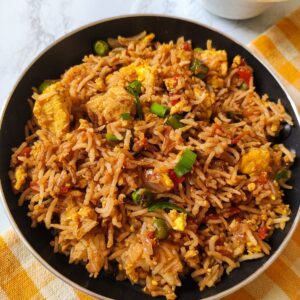 tofu fried rice served in a black pan kept on a table napkin with yellow and white checks