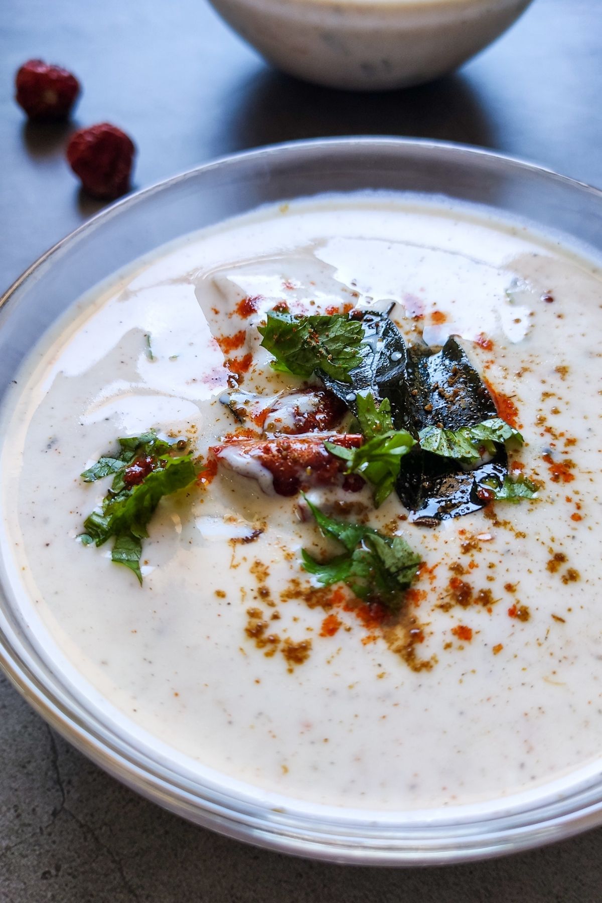 aloo raita garnished with curry leaves, cilantro and spices served in a glass bowl