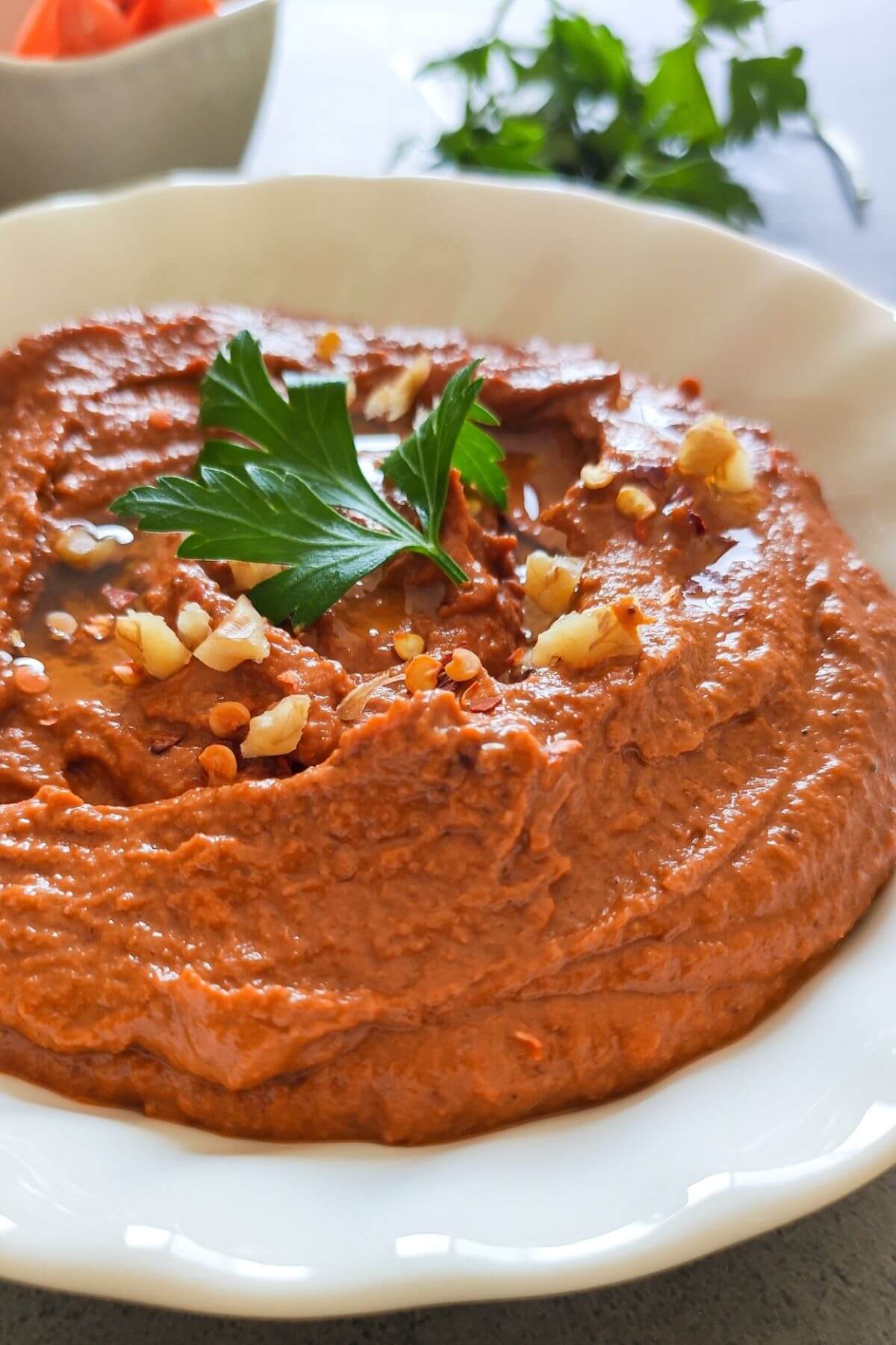Lebanese muhammara garnished with chopped walnuts and parsley in a white bowl