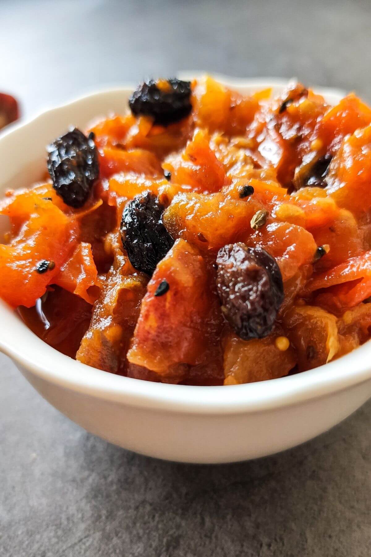 Bengali sweet tomato date chutney with black raisins in a white bowl