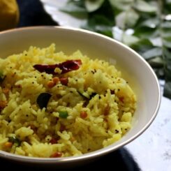 lemon rice served in a white bowl with curry leaves and lemon in the background