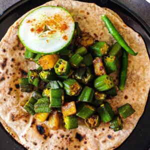 Aloo bhindi served on top of a roti with a slice of cucumber and two green chilies