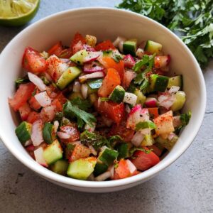 Kachumber salad in a white bowl with lime slice and fresh cilantro in the background