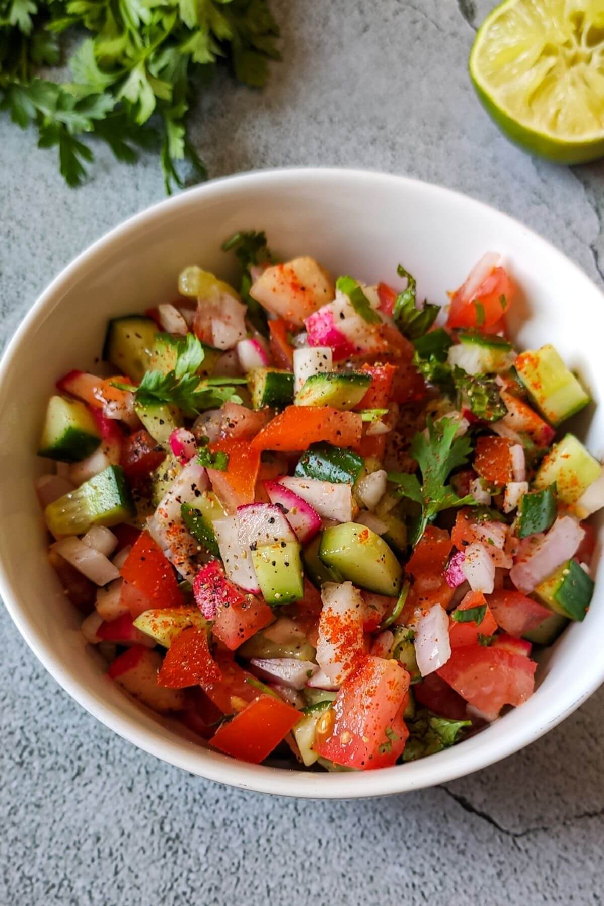 Spicy Indian cucumber tomato salad served in a white bowl with a slice of lime and fresh cilantro in the background