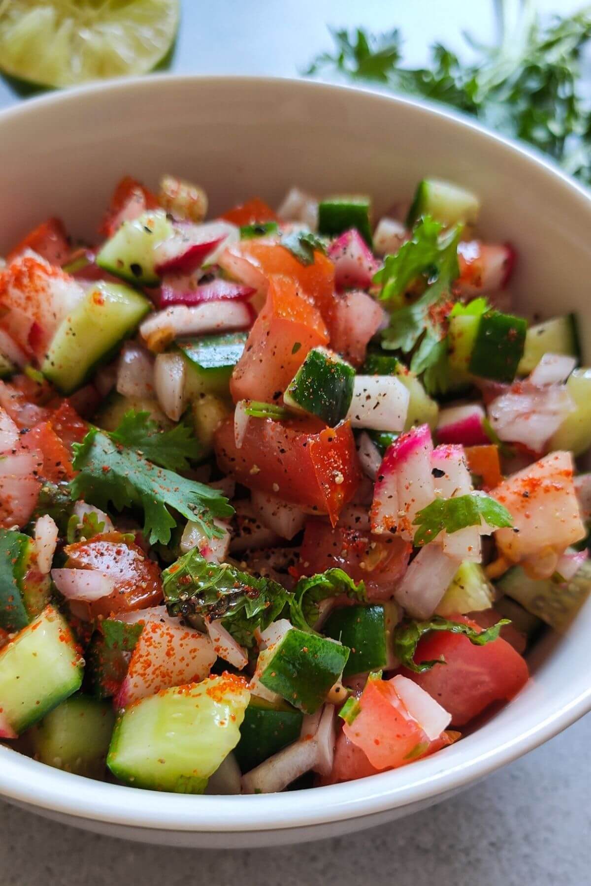 Indian vegetable salad served in a white bowl with cilantro and a slice of lime visible in the background