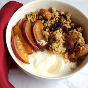 a bowl with home made granola, yogurt, and fresh cut plums