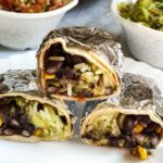 Three vegan burritos placed on top of each other, served in a white plate with salsa and Guacamole
