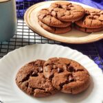 Two vegan chocolate coffee cookies served on a white plate with more cookies in the background