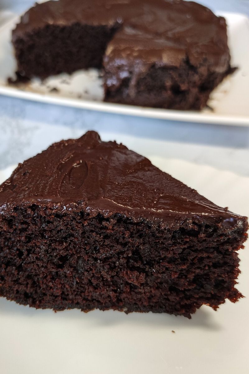 a slice of vegan chocolate cake served on a white plate and remaining cake kept in the background