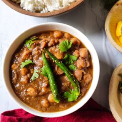 vegan chickpea curry served in a white bowl with rice, lemon wedges, and fried green chilies