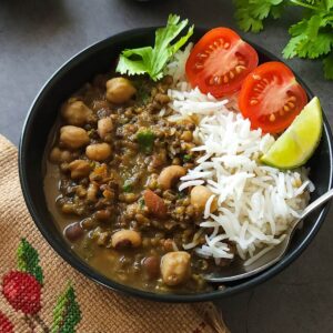 Indian mixed beans curry with rice and salad served in a black bowl.