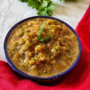 Tomato chutney served in a bowl with coriander leaves in the background