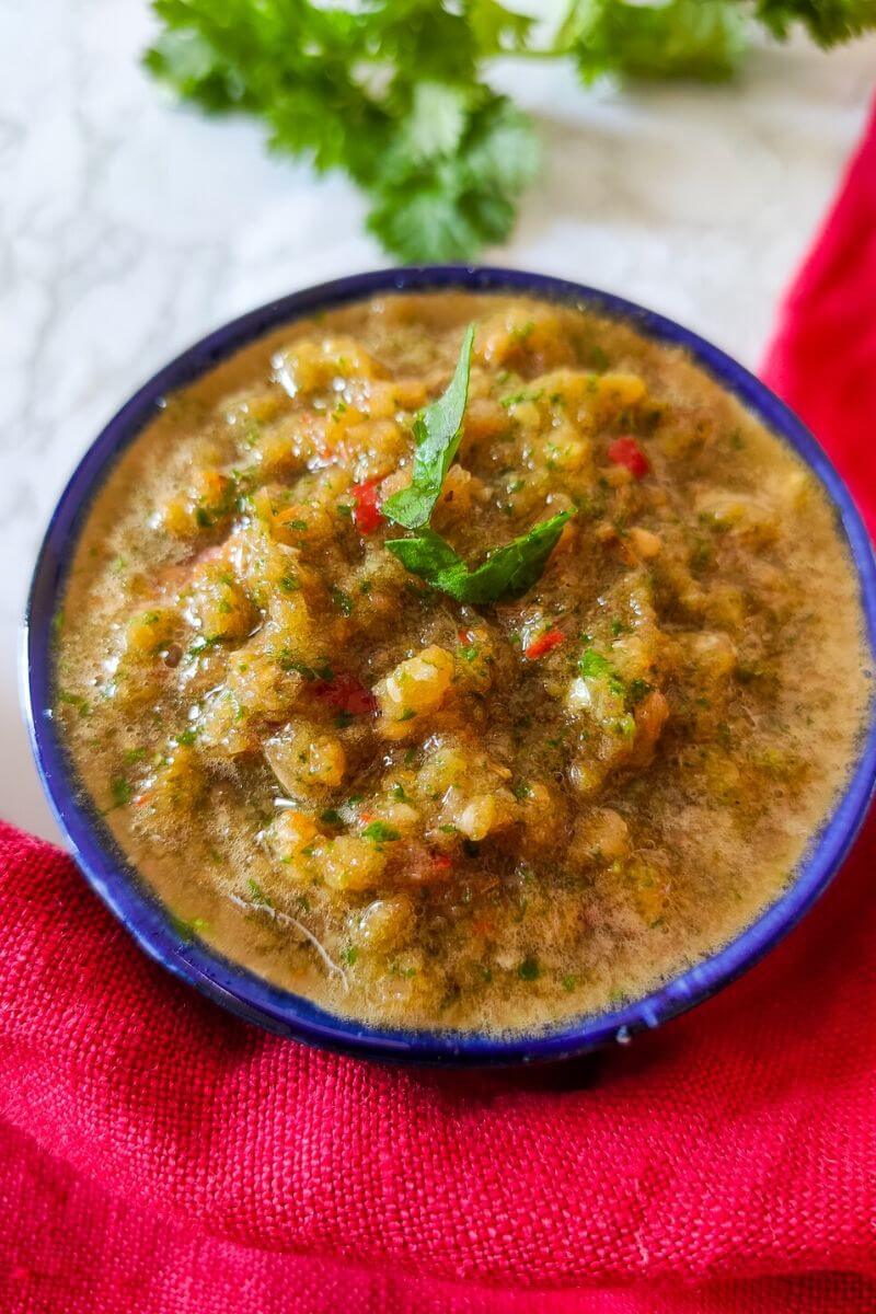 Tomato chutney served in a bowl with coriander leaves in the background
