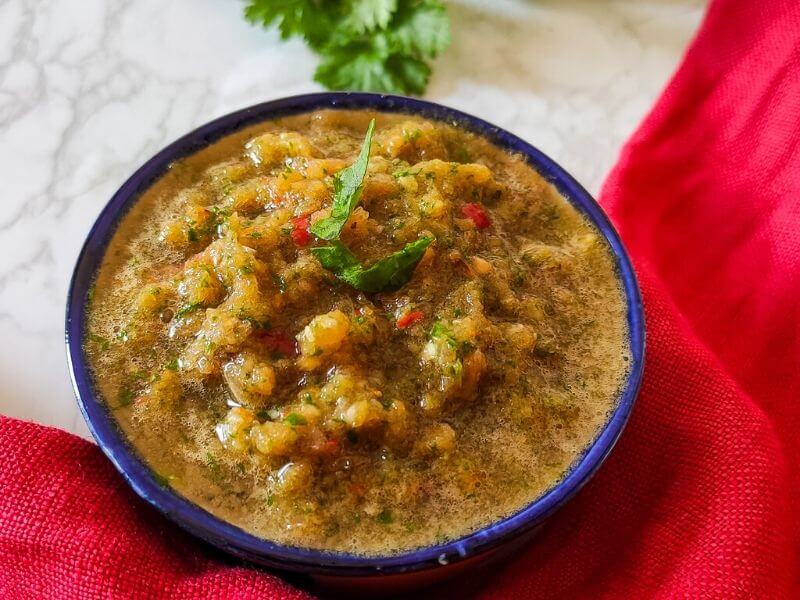 Tomato chutney served in a bowl with coriander leaves in the background