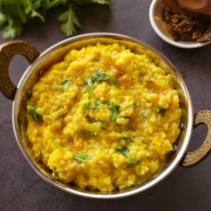 Moong dal Khichdi in a small wok with a bowl of pickle and cilantro in the background.