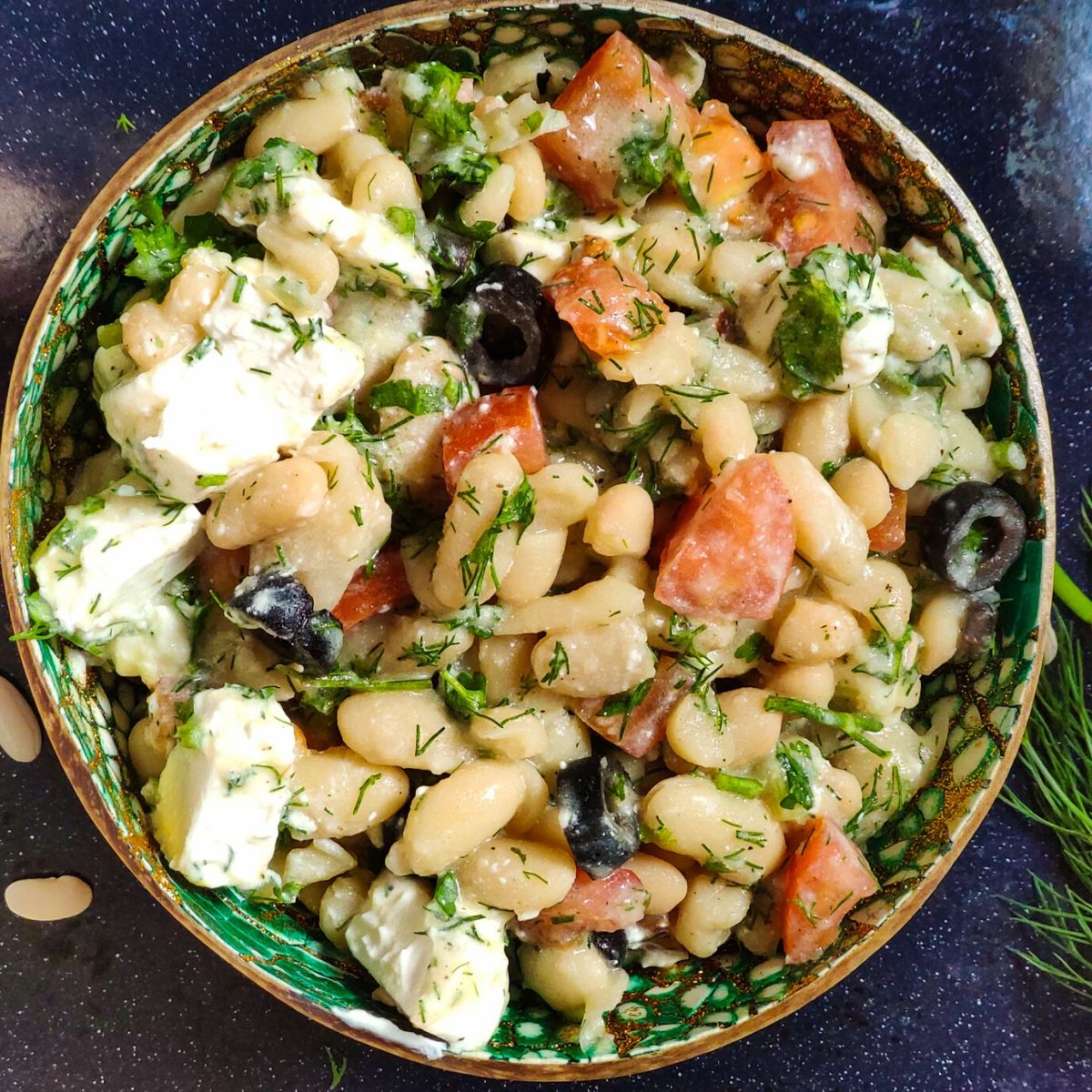Mediterranean white bean salad served in a green bowl with fresh dill and dried white beans in the background